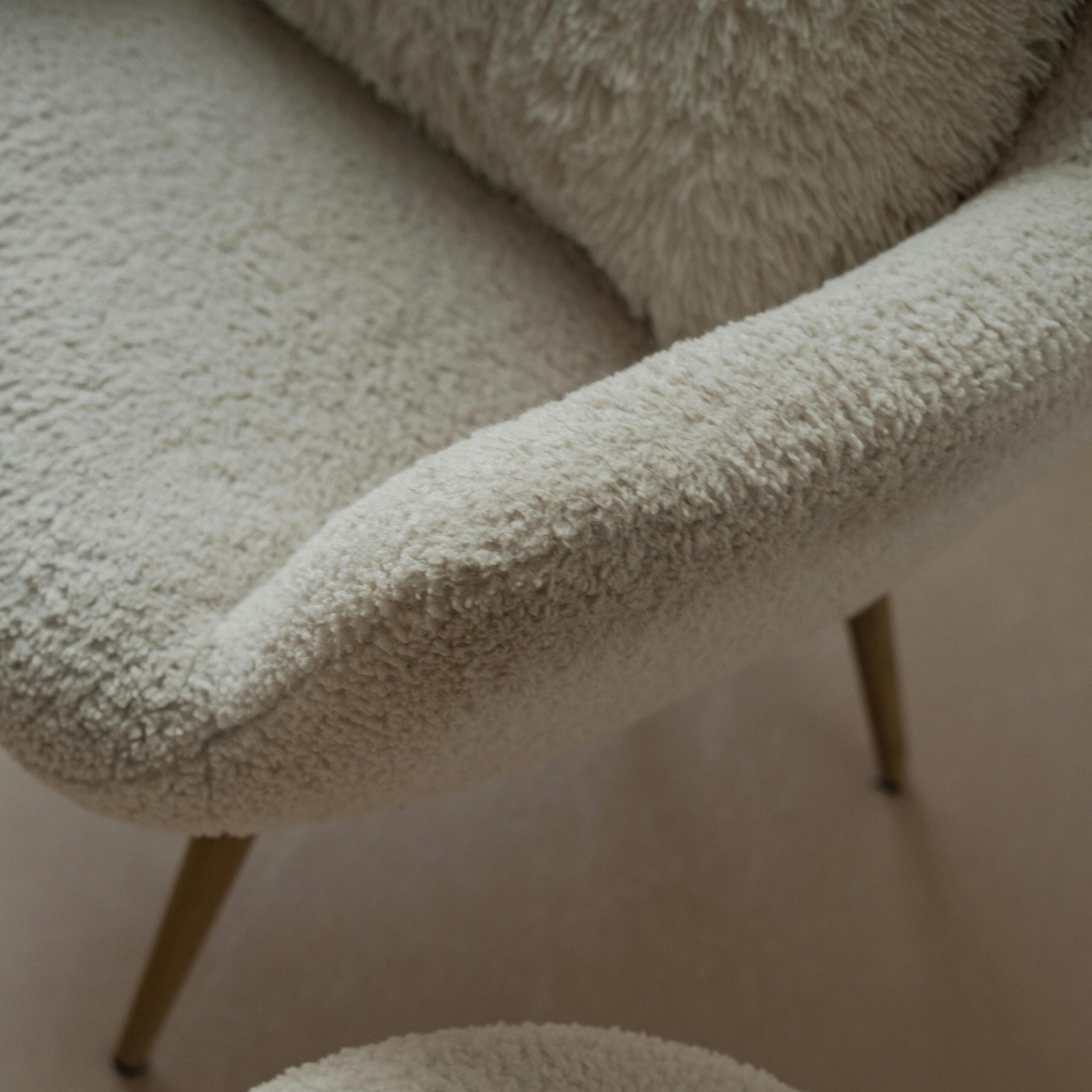 A warm and inviting space with a white sherpa armchair and a laptop on a footstool, perfect for a cozy workspace.